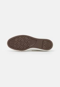 Weißer Sneaker mit einer braunen Gummisohle, die ein strukturiertes Grip-Muster, eine umrandete Kante und minimale Branding-Details aufweist.