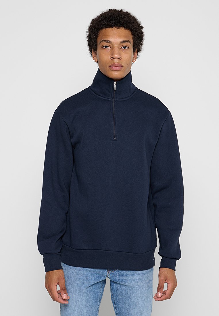 Sweat-shirt bleu marine à fermeture éclair quart en tissu doux, avec un col montant, des poignets et un ourlet côtelés. Coupe décontractée et confortable sans motifs.