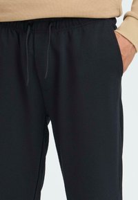 Mustat collegehousut, joissa on teksturoitu kangas, joustava vyötärö ja nyöri. Sivutaskut ja rento istuvuus.