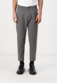 Gray chinos with an elastic waistband, button closure, and tapered legs. Worn with black socks and slip-on shoes, featuring a shiny finish.