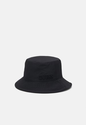 Czarna czapka typu bucket z szerokim rondem i subtelnie wyszywanym logo "GUESS" z boku na jednolitym jasnym tle.