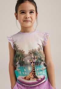 Lila majica s nabranimi rokavi, ki prikazuje grafiko žirafe v sončnih očalih na plovilu, postavljeno pred ozadje bazena ob palm.