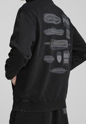 Svart sweatshirt med relaxed passform, med tonala grafik och logotyper på baksidan. Ribbstickade muddar och fåll för extra textur.