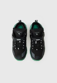 Fekete sportcipők zöld részletekkel, texturált szintetikus felsőrész, állítható pánt és fekete fűzők. Párnázott talpbetéttel felszerelve.