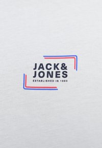 Valkoinen puuvillainen t-paita, jossa on "JACK & JONES" -logo tummansinisellä, punaisilla ja sinisillä reunaviivakorostuksilla. Tekstissä lukee "ESTABLISHED IN 1990."