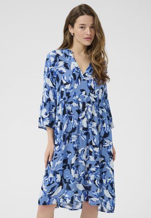 Modra cvetlična obleka z V-izrezom, rokavi do tričetrt, in nabranimi plastmi. Značilne so različne odtenke modre in črne v mehkematerialu.