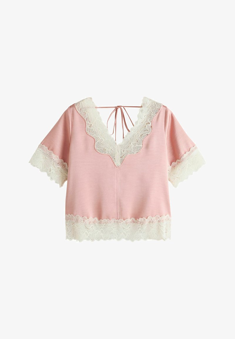 Blouse rose à manches courtes avec bordure en dentelle blanche sur le col en V, les manches et l'ourlet, avec une fermeture à nouer dans le dos.