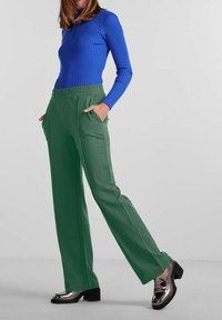 Długie zielone spodnie z bocznymi kieszeniami, zestawione z dopasowanym, prążkowanym niebieskim topem. Czarne buty na obcasie z błyszczącymi akcentami dopełniają strój.