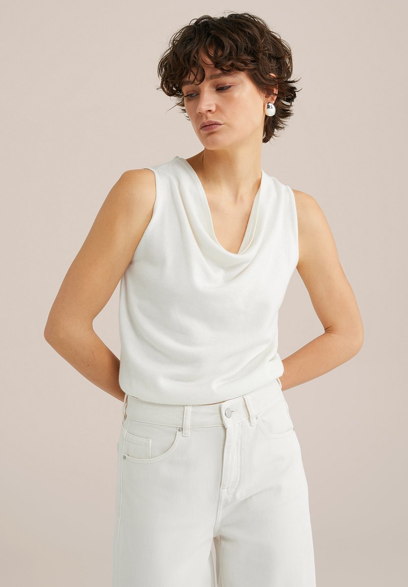 Top blanco sin mangas con escote drapeado, textura suave, combinado con jeans blancos de tiro alto en un corte relajado.