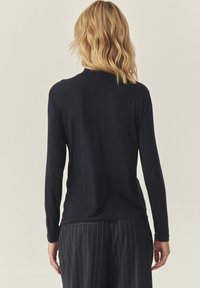 Mornarica dugi rukav s uskim siluetom, mekanim materijalom i okruglim izrezom, u kombinaciji s hlačama na pruge. Pogled sa stražnje strane.