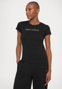 Camiseta de algodón negra con mangas cortas y cuello redondo. Presenta un logotipo gráfico blanco, "ARMANI EXCHANGE", centrado en el pecho.