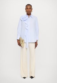 Ανοιχτό μπλε oversized πουκάμισο με φουσκωτές λεπτομέρειες και λο�υλουδάτο σχέδιο στον ώμο, συνδυασμένο με κρεμ παντελόνι σε φαρδιά γραμμή και χρυσό τσαντάκι.