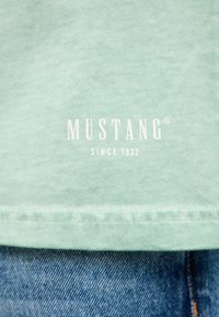 Mint-green cotton t-shirt with white "MUSTANG" logo and "SINCE 1932" below, featuring a clean, simple design and visible stitching at the hem.