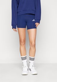 Námořnicky modré sportovní šortky s přiléhavým střihem a bílým logem Adidas. Doplněné podkolenkami bílými s černými pruhy a černými doplňky.