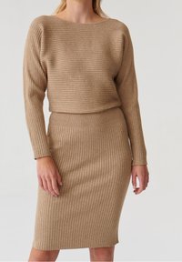 Tvådelat stickat set med ribbad textur, långa ärmar och båturringning. Tyget är i en varm beige nyans med en figurnära passform.