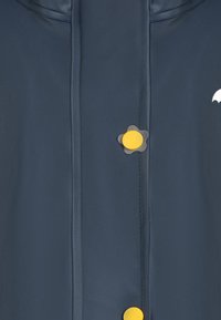 Jūrinis vandeniui atsparus švarkas su apvalia apykakle, priekinis mygtukų užsegimas su geltonu gėlelės formos mygtuku ir mažas baltas logotipas ant peties.