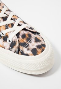 Zbliżenie na sneaker z białymi sznurówkami, grubą fakturowaną białą podeszwą i górą z tkaniny w wzór lamparta.