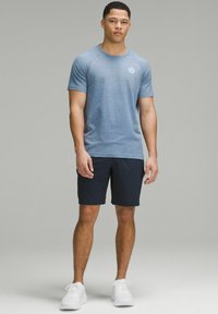 Men's athletic outfit featuring a light blue textured short-sleeve shirt and dark shorts, complemented by white sneakers.