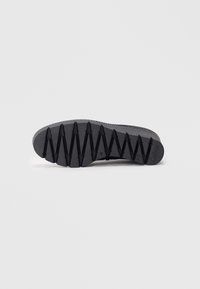 Semelle de chaussure noire en caoutchouc texturé, dotée d'un motif en zigzag pour une meilleure adhérence et d'une marque distinctive au niveau du talon.