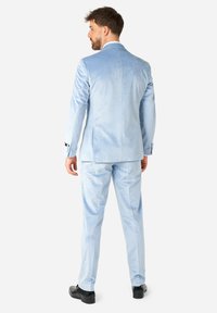 Traje de terciopelo azul claro con un corte ajustado, chaqueta de un solo botón y pantalones a juego. Zapatos negros completan el atuendo.