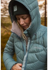 Lichtblauwe geïsoleerde jas met een capuchon, voorzien van een gequiltte structuur en een subtiele decoratieve afwerking. Warme grijze binnenvoering.