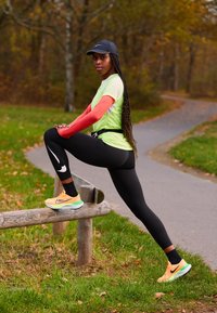 Femme en tenue de sport vive étirant une jambe sur une barrière en bois le long d'un sentier sinueux dans un parc en automne.