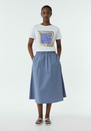 White t-shirt with a blue, green, and gold patterned graphic paired with a gray midi skirt featuring an elastic waistband and side pockets.