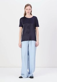 Top corto in satin blu navy abbinato a pantaloni a gamba larga azzurri. L'outfit è completato da scarpe nere e un design minimalista.