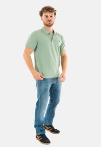 Polo de manga corta verde claro, combinado con jeans de mezclilla azules y zapatillas negras con acentos naranjas. Diseño simple y clásico.