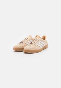 Beige mockaskor med vita ränder och en gummisula. Snörningsdesignen har en texturerad tå och en vadderad krage för komfort.