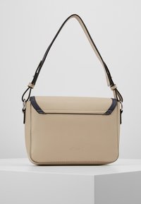 Beige nahkakäsilaukku mustalla yksityiskohdalla kannessa, joka sisältää yhden olkahihnan ja minimalistisen muotoilun. Sujuva pinta.