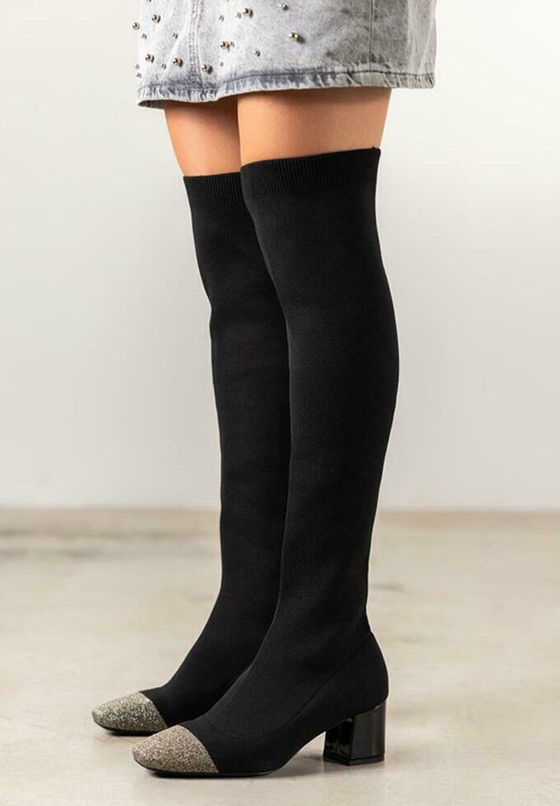 Botas de punto negras hasta la rodilla con un tacón grueso, que presentan una puntera metálica plateada en forma de punta y una textura suave.