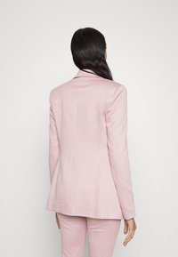 Blazer a motivi houndstooth rosa con una vestibilità sartoriale. Presenta spalle strutturate e una fessura singola sul retro per facilitare i movimenti.