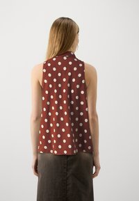 Top sin mangas de tejido en color óxido con grandes lunares blancos, cuello redondeado y corte holgado, combinado con una falda de mezclilla oscura.