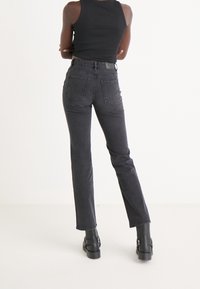 Svarta raka jeans i denim, med två bakfickor, hög midja och subtila sömmar. Bärs med kraftiga svarta kängor.