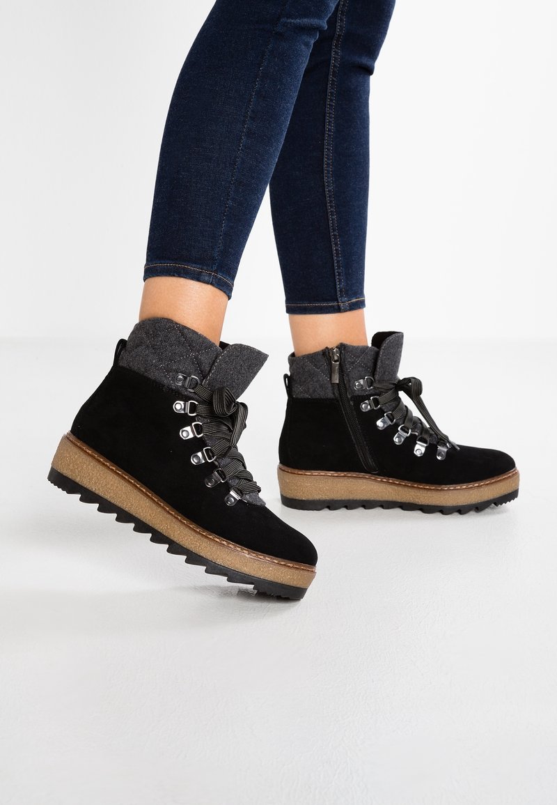 Botas de tobillo de ante negro con cuello de fieltro gris, parte delantera con cordones, ojales de metal y suela gruesa y texturizada con una plantilla intermedia marrón en contraste.