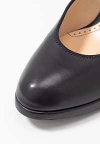 Černé kožené baletní střevíce s zaoblenou špičkou a hladkým povrchem na bílém pozadí, zobrazující detaily zvrchu a z boku.