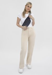Beige high-waisted jeans met een rechte pijp, gecombineerd met een witte aansluitende t-shirt en een marineblauwe schoudertas met gouden rits en banden.