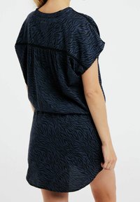 Laivastonsininen mekko mustalla seepri raidalla, lyhyillä hihoilla ja rentoa mittaa. Pehmeä kangas, jossa on kaarrettu helma ja hieman läpikuultava rakenne.