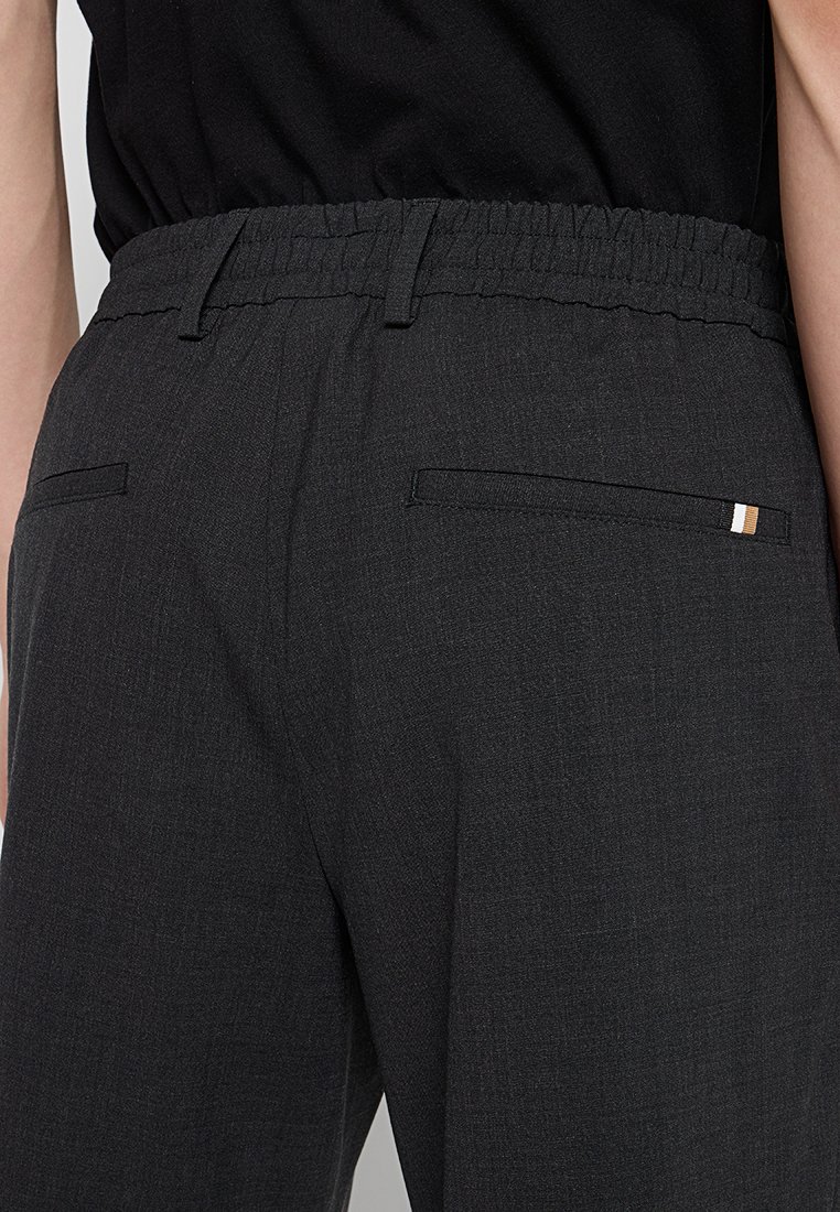 Dunkelgraue Pants mit elastischem Bund und strukturierter Oberfläche, ausgestattet mit zwei Gesäßtaschen und einem kleinen gestreiften Akzent auf der rechten Tasche.