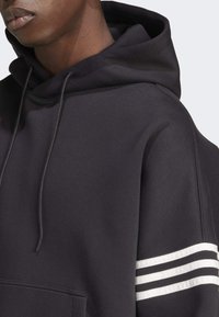 Sudadera negra con capucha, presenta un cordón, un bolsillo canguro y un acabado texturizado con acentos de tres franjas blancas en las mangas.