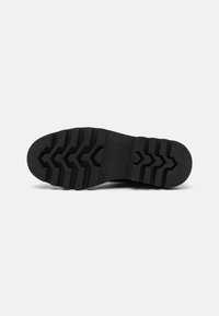 Semelle de chaussure en caoutchouc noir présentant un motif de semelle en zigzag pour une traction et une durabilité. La semelle est plate avec des rainures et des crêtes bien définies.