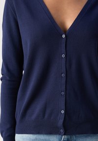 Námořnický cardigan s výstřihem do V, dlouhými rukávy a šesti malými knoflíky vpředu. Hladká textura s ribbovaným lemem.