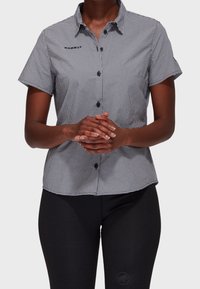 Camicia a maniche corte a quadrettoni bianco e nero con frontale a bottoni, dotata di tasca e bottoni neri a contrasto.