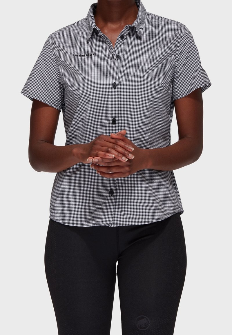 Camicia a maniche corte a quadrettoni bianco e nero con frontale a bottoni, dotata di tasca e bottoni neri a contrasto.