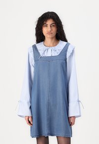 Denimkjole med firkantet utringning og sidesømmer, med en blåstripet bluse under med volanger på ermene og knyttede mansjetter.