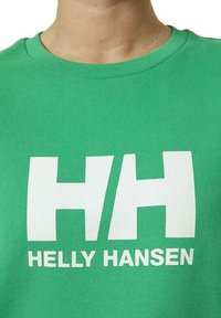 Sudadera verde con cuello redondo que presenta un gran logo blanco "HH" y el texto "HELLY HANSEN". La tela parece texturizada y suave.