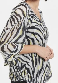 Černobílá průsvitná blůza s odvážnými pruhy zebra a krátkými rozšířenými rukávy. Má výstřih do V a uvolněný střih.