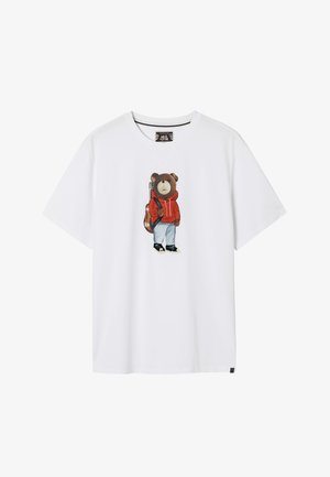 Valkoinen puuvillainen t-paita, jossa on piirros karhusta punainen huppari päällä, vaaleansiniset farkut ja mustat kengät, kitaran roikkuessa olkapäällä.
