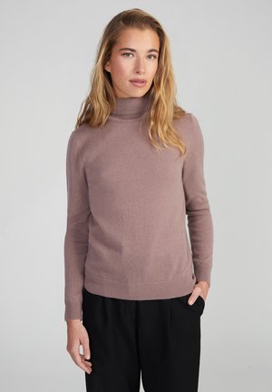 Helllila Rollkragenpullover aus weichem Strickstoff mit gerippten Bündchen und Saum, kombiniert mit lockeren schwarzen Hosen.